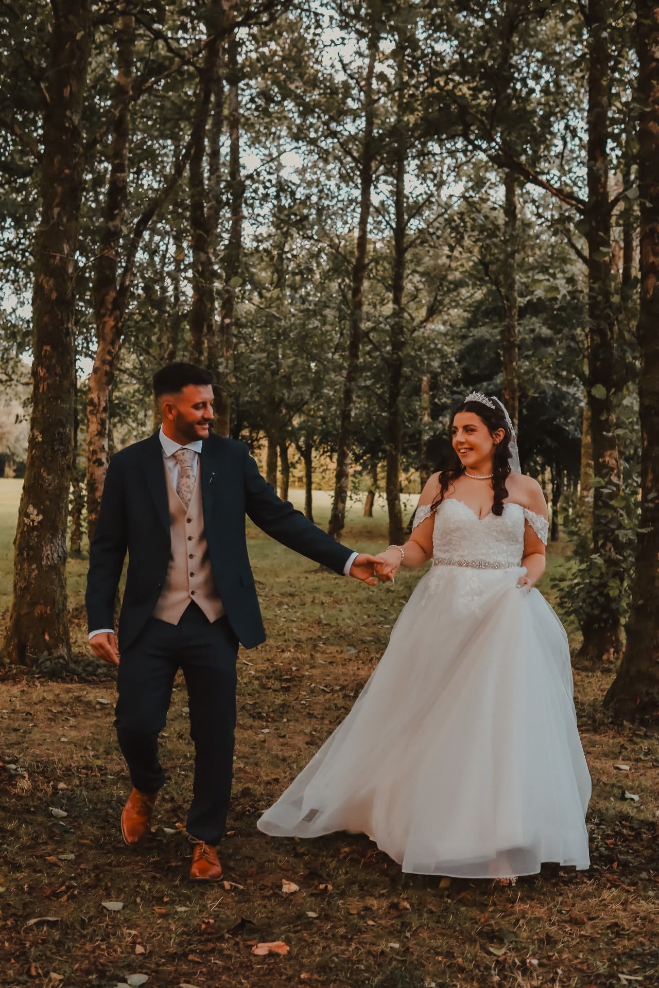 Bride and groom walking hand in hand through a sunlit woodland clearing