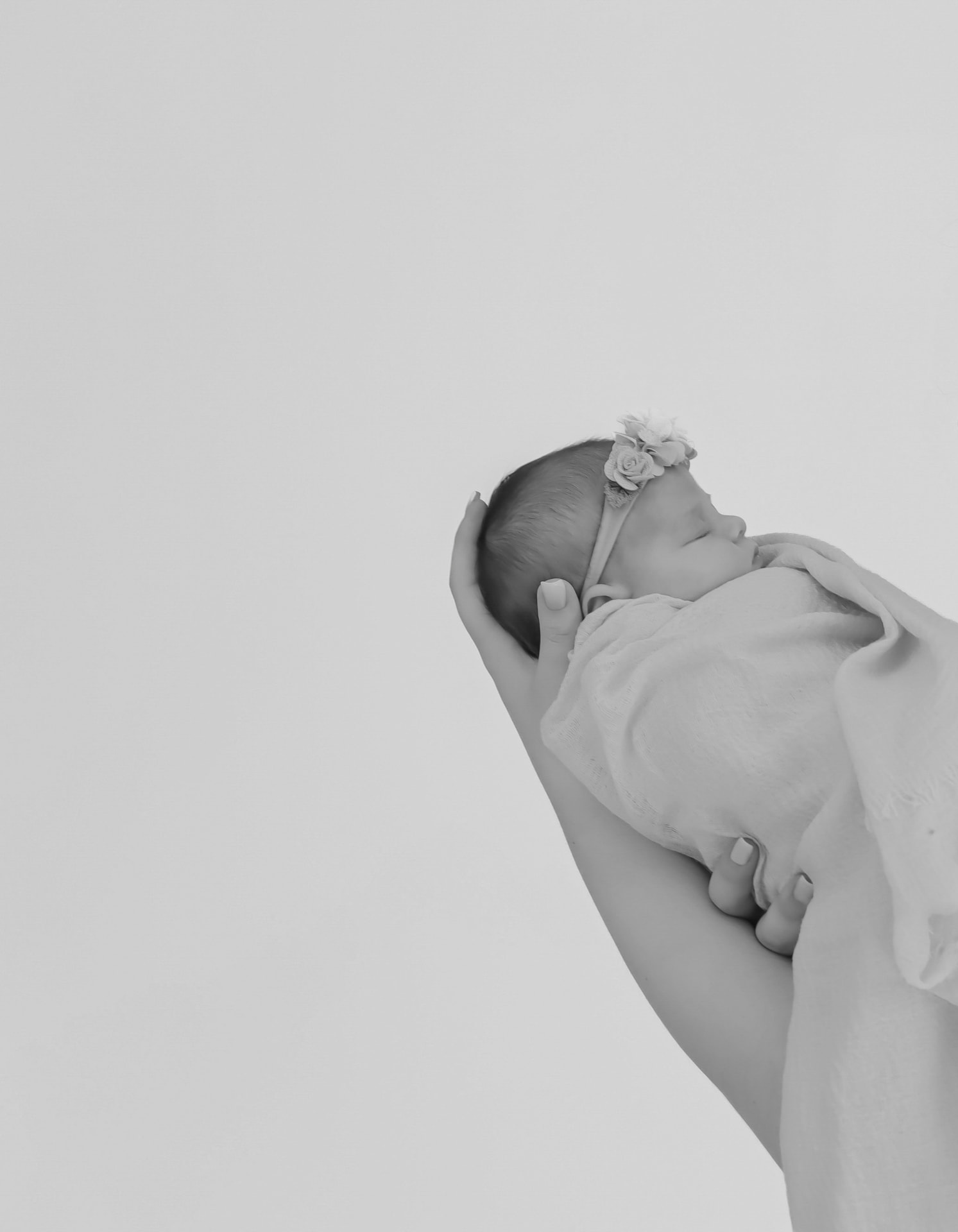 Black and white close-up of a sleeping newborn in a floral headband, held tenderly