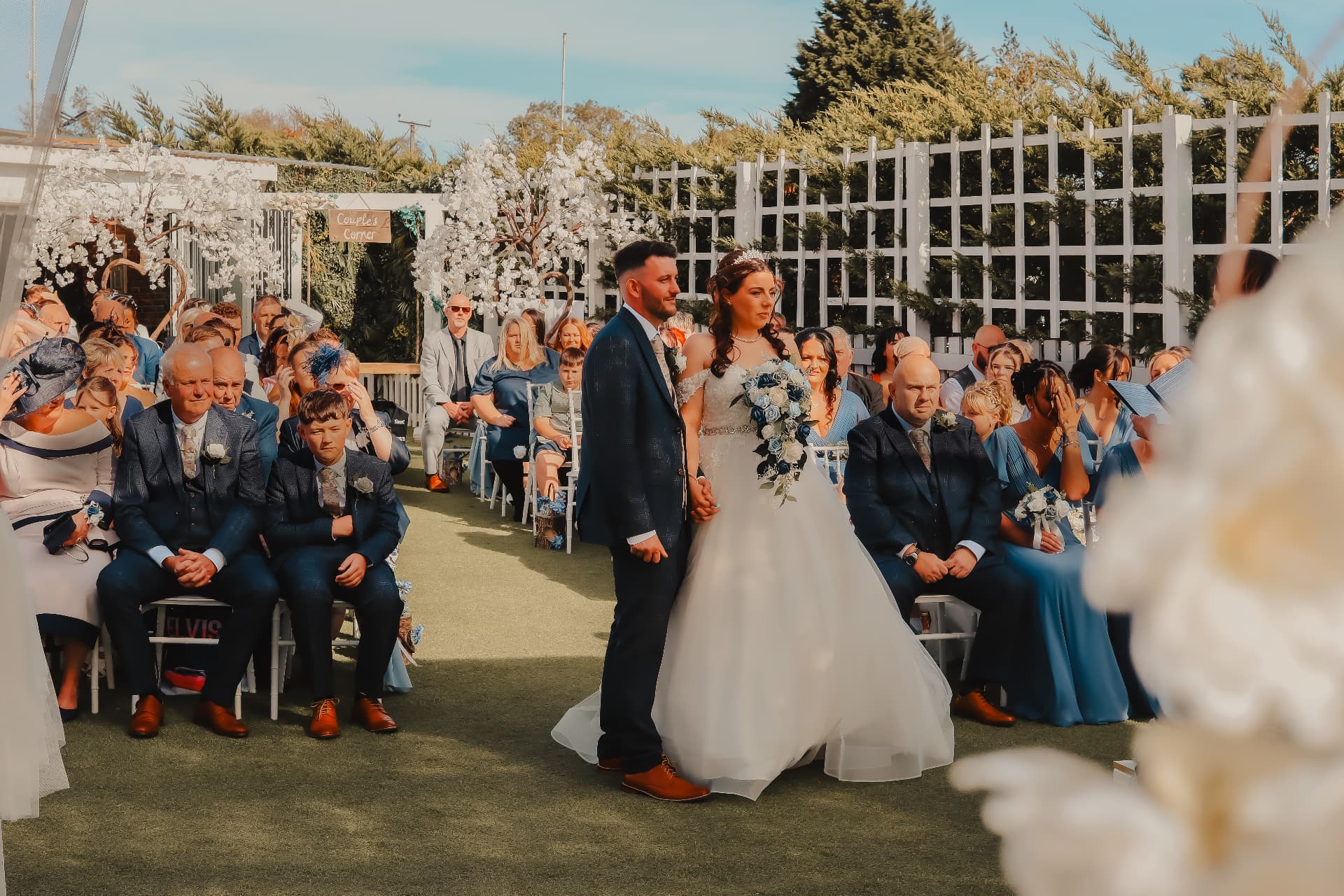Bride and groom standing together at an outdoor ceremony surrounded by family and friends
