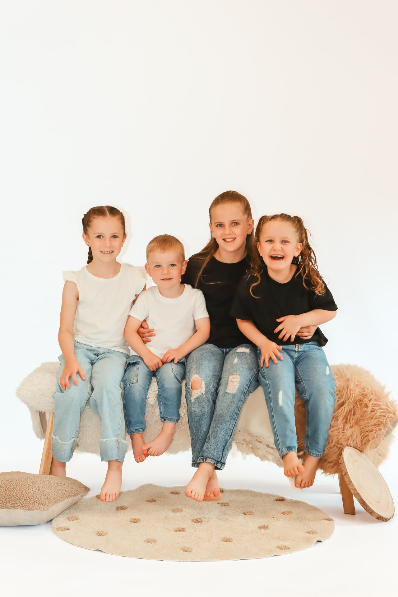 Four siblings sitting together laughing on a bright studio backdrop