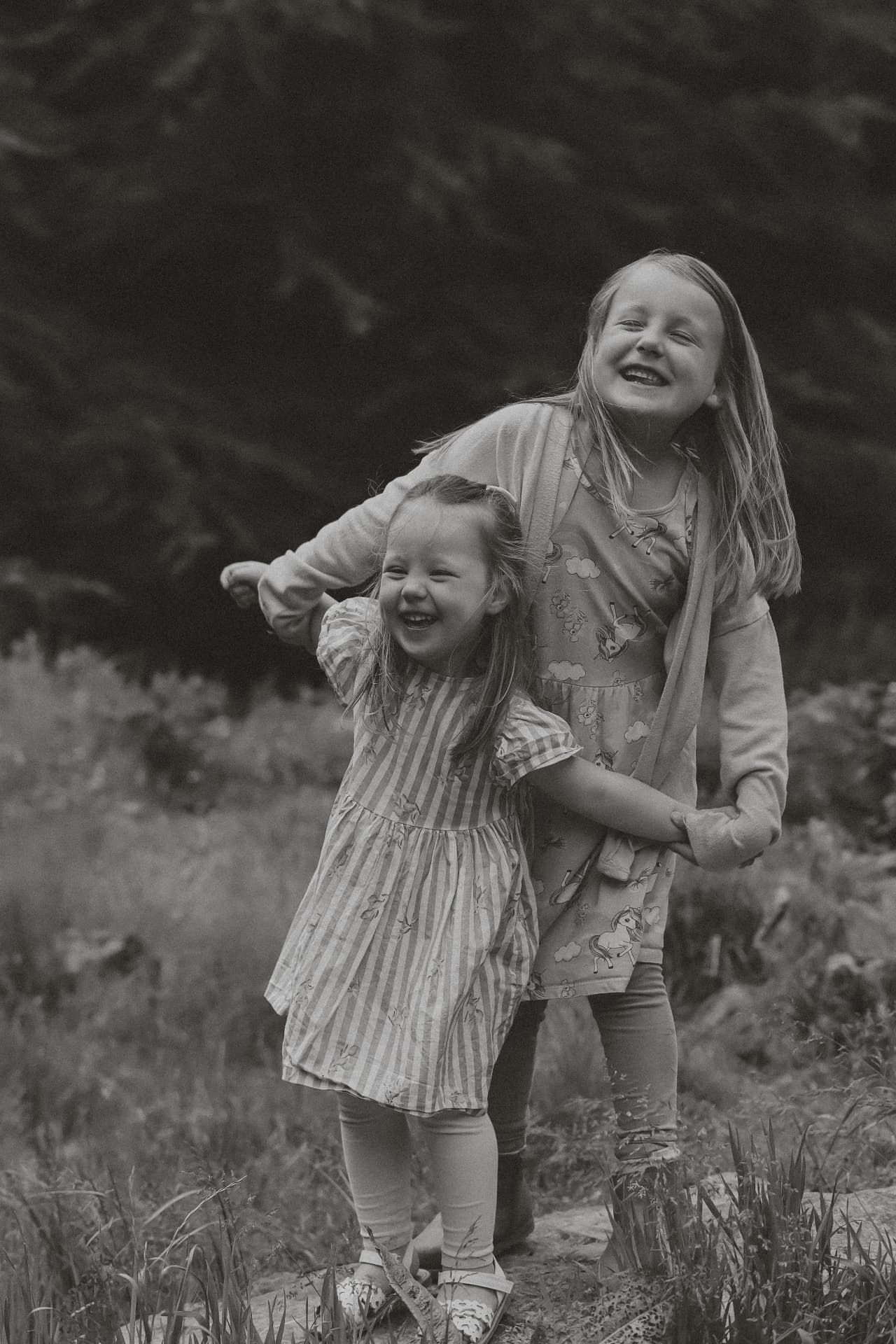 Black and white photograph of two sisters laughing together in a woodland clearing