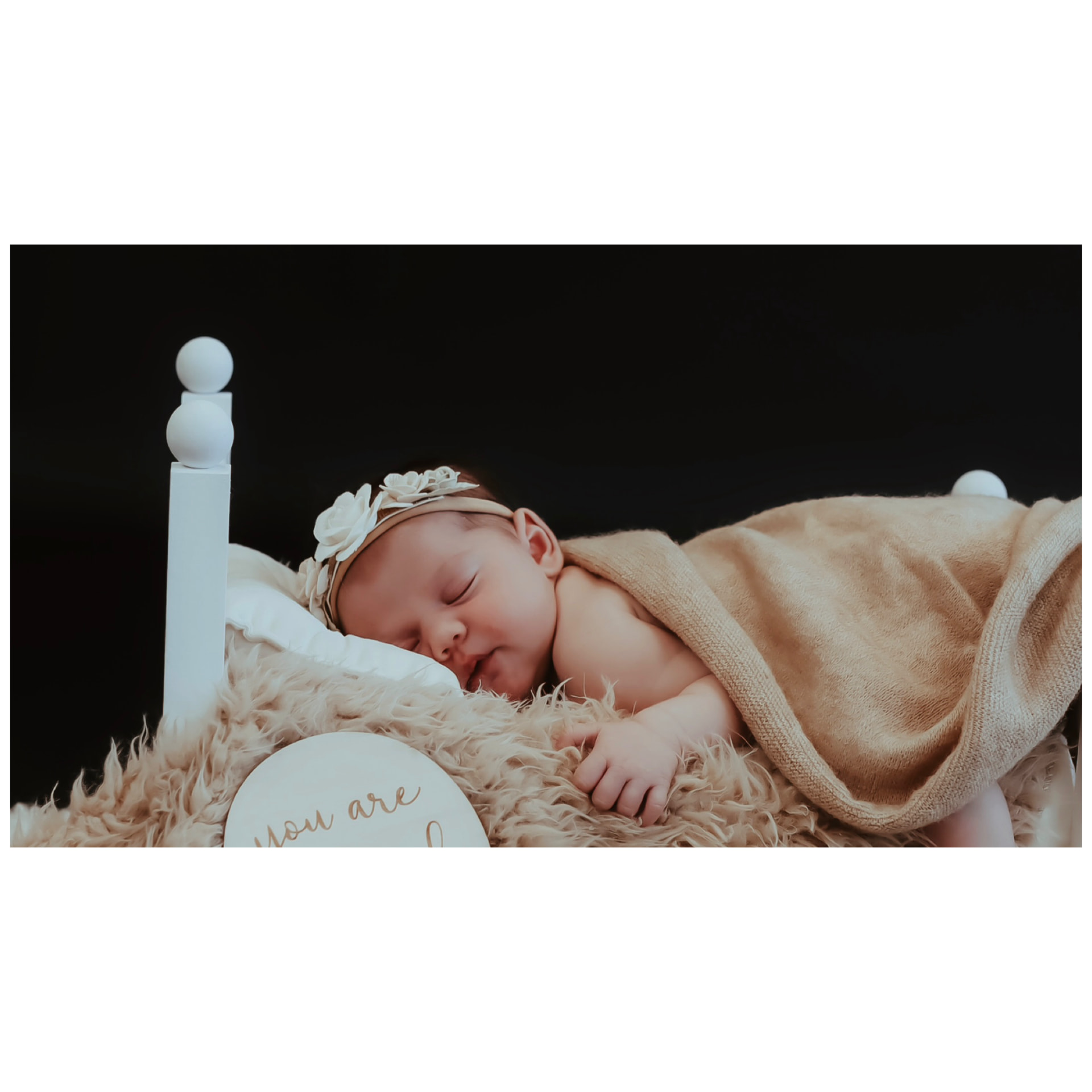 A sleeping newborn nestled on a fluffy bed with a 'you are loved' keepsake sign