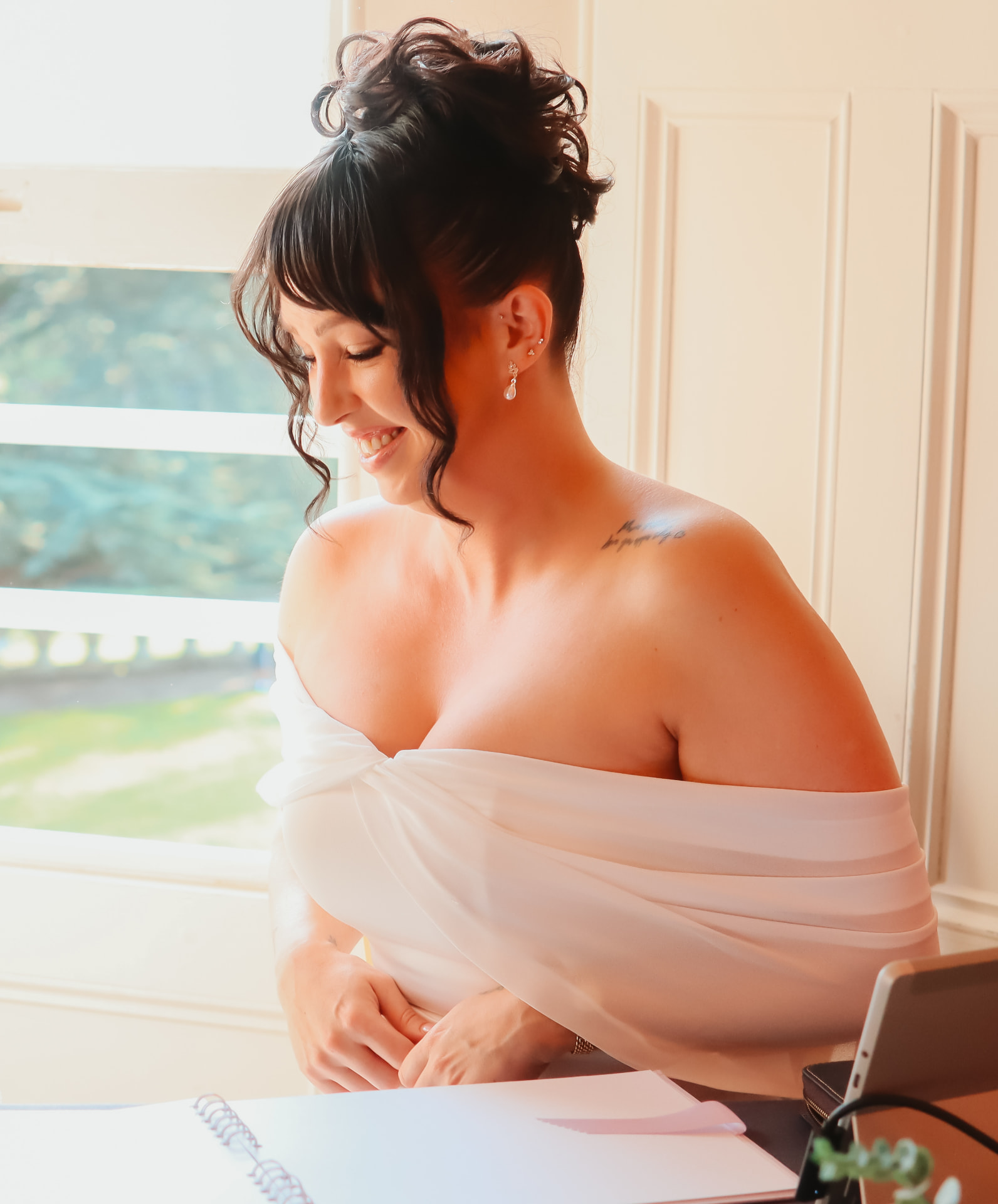 Bride smiling softly by a bright window during morning preparations
