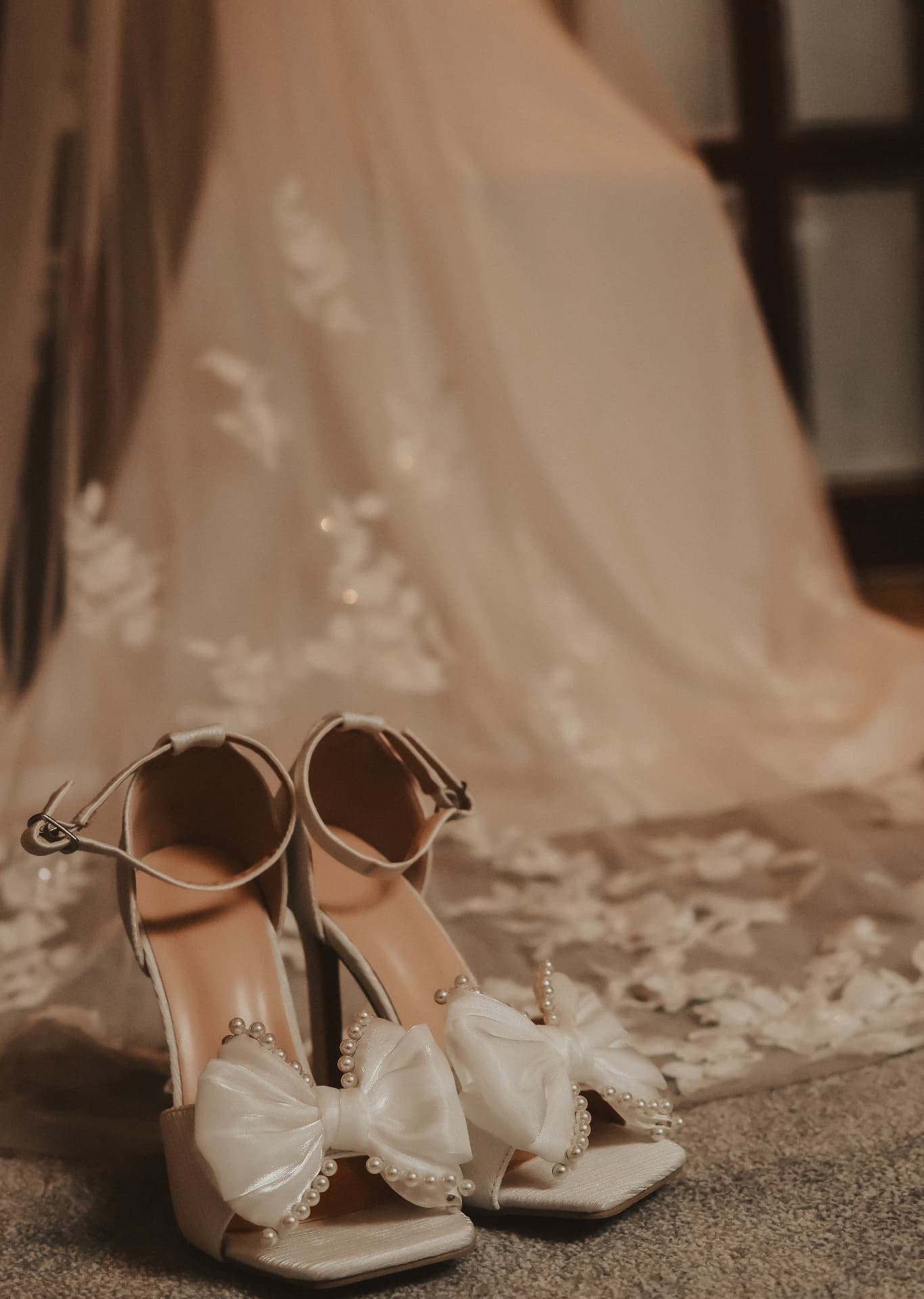Bridal shoes with pearl bows resting beside the veil in warm morning light